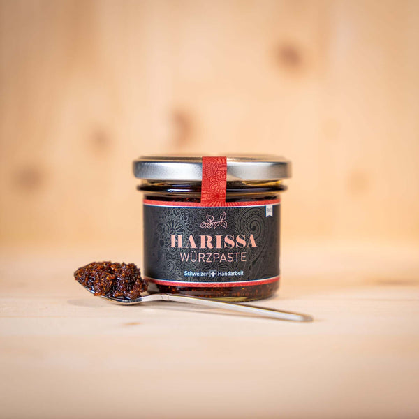 BIO Harissa Würzpaste im Glas, serviert mit einem Teelöffel auf hellem Holzuntergrund.