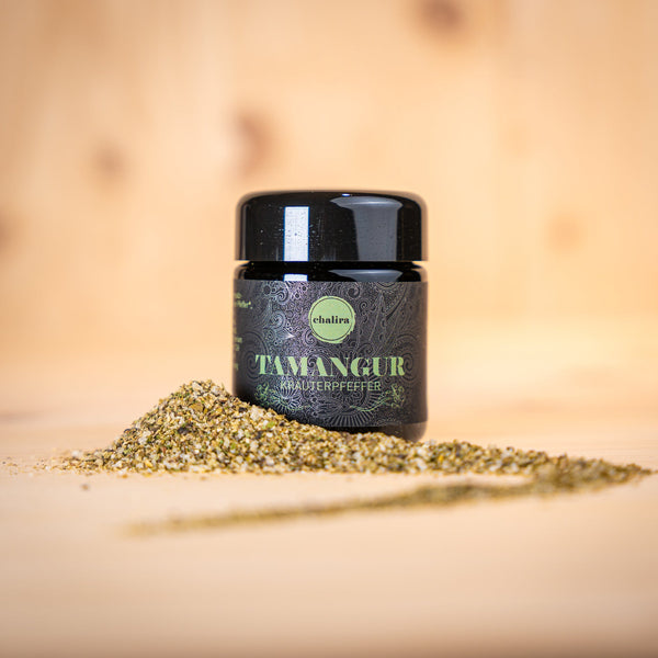 TAMANGUR BIO Kräutersalz La Pesteda im Glasbehälter, umgeben von gewürztem Salz auf Holzuntergrund.